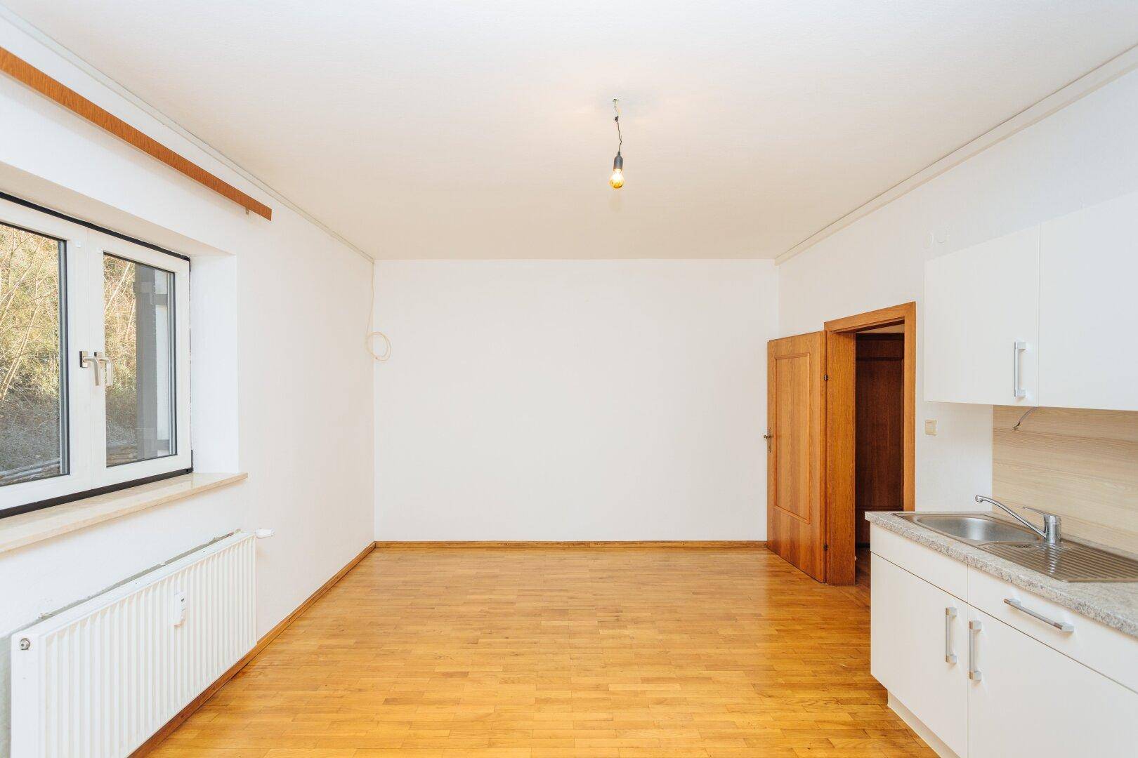 Heller Raum mit Parkettboden und integrierter Küchenzeile, ideal für ein Studioapartment.