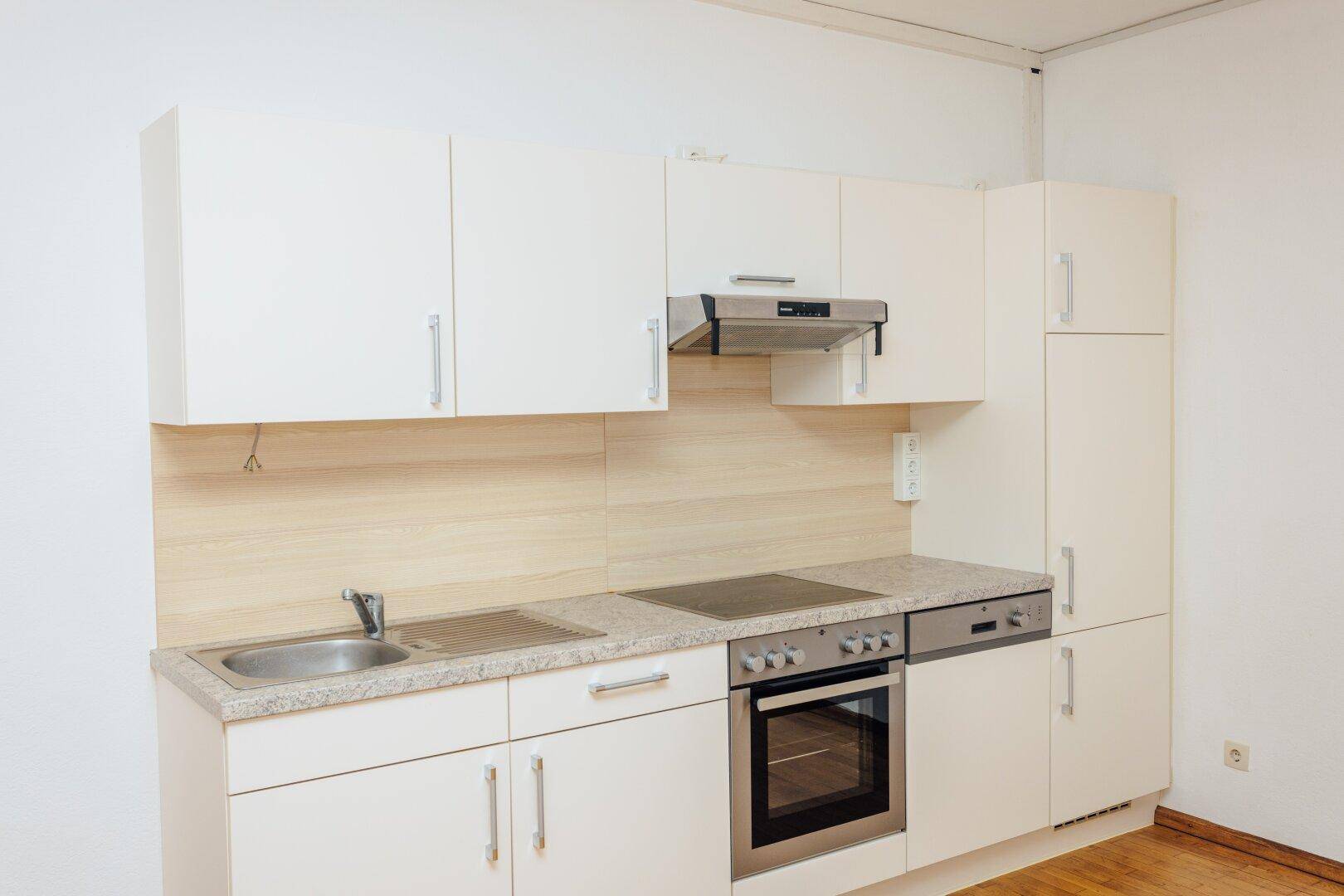 Helle Einbauküche mit weißen Schränken, integriertem Backofen, Kochfeld und Spülmaschine.