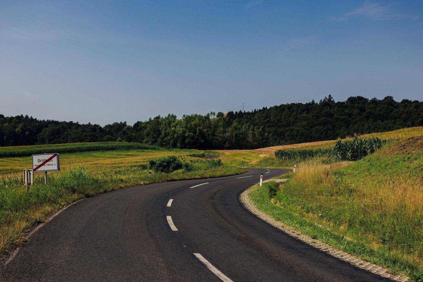 Kurvenreiche Landstraße schlängelt sich durch eine ländliche Landschaft mit Feldern und Wäldern.