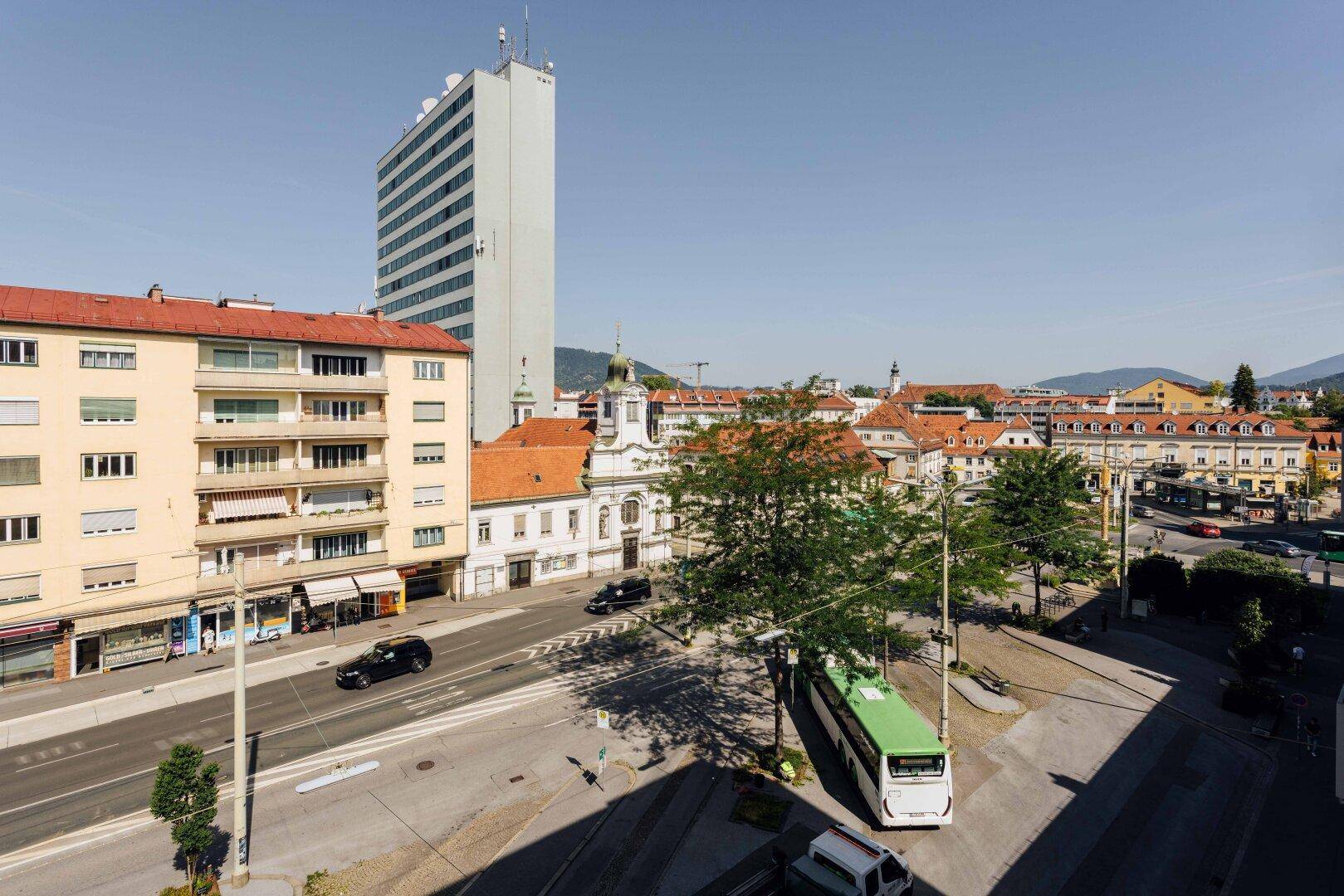 Weitläufiger Stadtblick mit einem hohen Gebäude, historischen Bauten und Verkehr.