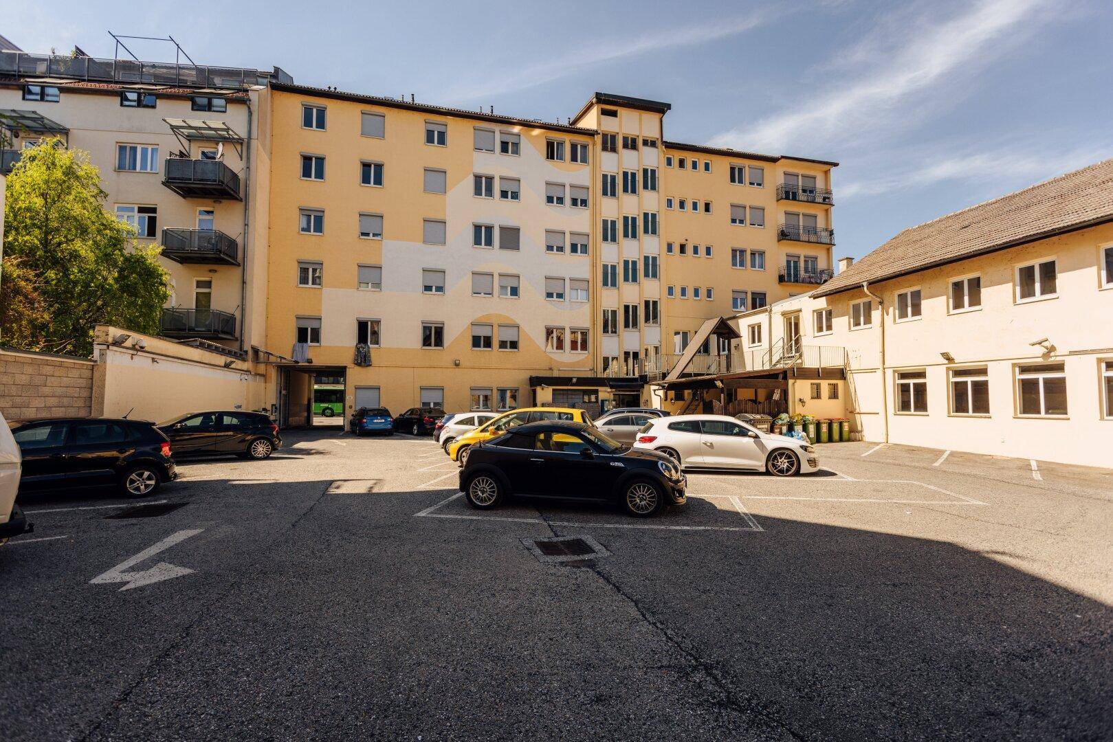 Blick auf den Außenparkplatz und die Rückseite des Mehrfamilienhauses mit weiteren geparkten Fahrzeugen.