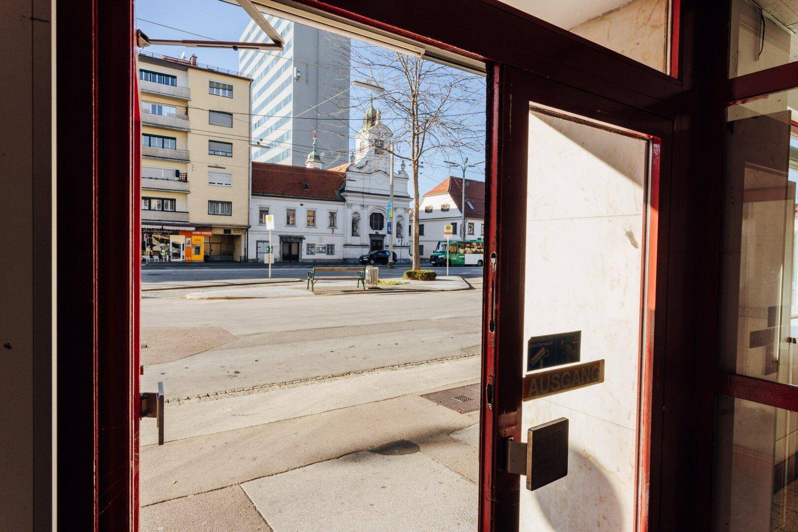 Eingangsbereich mit Blick durch die rote Tür auf die Straße und historische Gebäude.