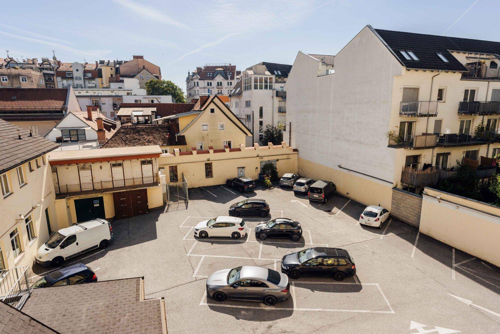 Außenparkplatz mit mehreren Autos, umgeben von Gebäuden und Dächern.