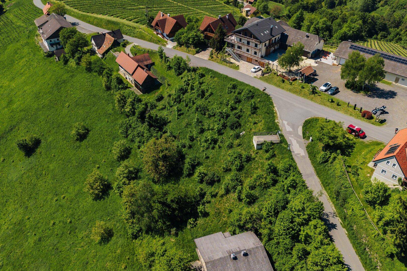 Schräge Luftaufnahme eines grünen Grundstücks mit umliegenden Häusern, Straßen und Weinbergen in der Landschaft.