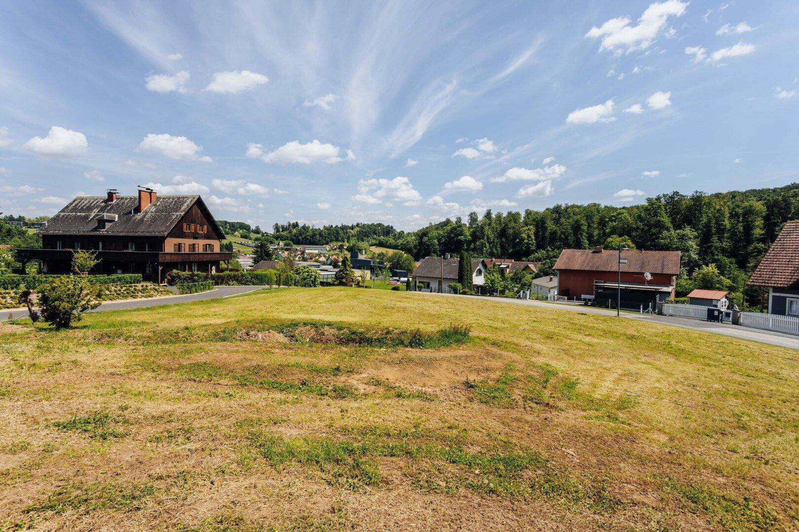 Unbebautes Grundstück in einer Wohngegend mit Blick auf umliegende Häuser und grüne Hügel.