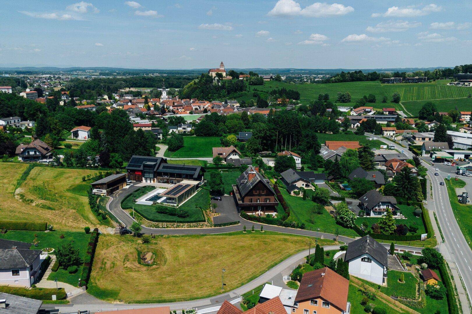 Luftaufnahme einer ländlichen Wohnsiedlung mit Häusern, Gärten und einem Schloss auf einem Hügel.
