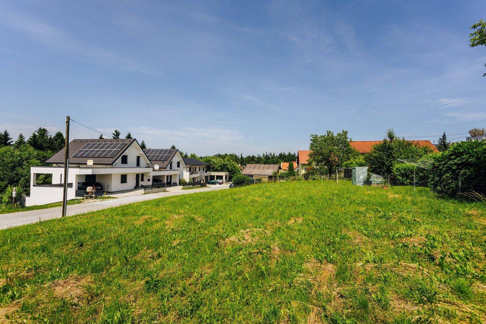 Grüne Wiese mit Blick auf moderne Einfamilienhäuser unter blauem Himmel.
