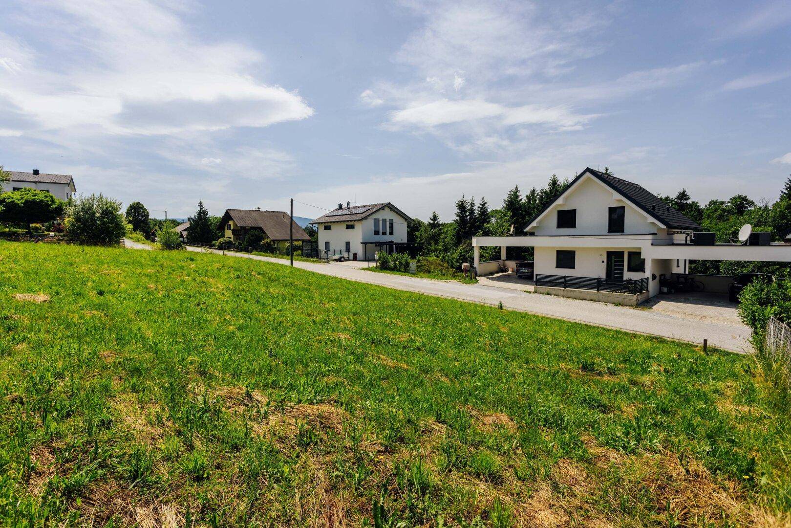 Weitläufige grüne Wiese mit mehreren Wohnhäusern und einem Carport im Hintergrund.