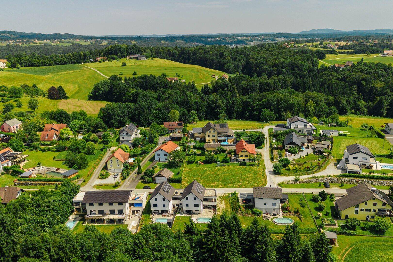 Weitläufige Luftaufnahme einer Wohnsiedlung eingebettet in eine grüne, hügelige Landschaft.