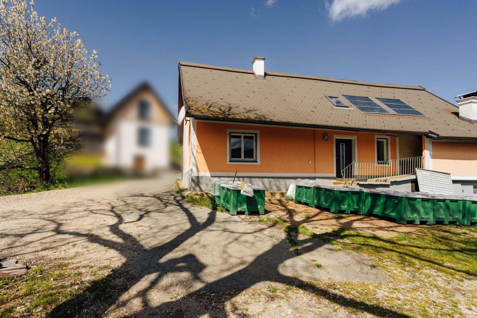 Haus mit orangefarbener Fassade, Solarpaneelen auf dem Dach und grünen Behältern im Vorgarten.
