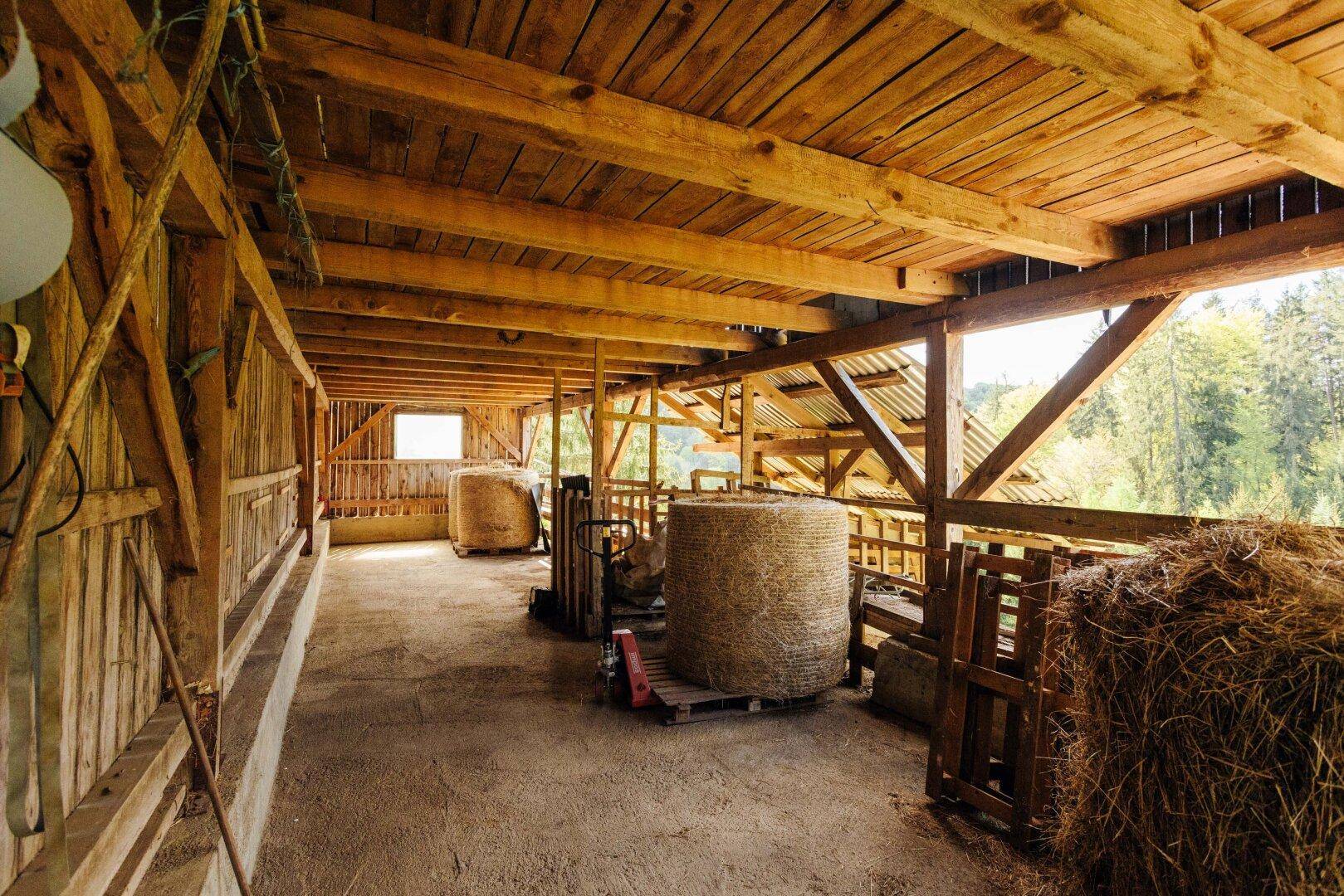 Innenansicht einer Holzscheune mit Heuballen, Holzbalken und natürlichem Lichteinfall.