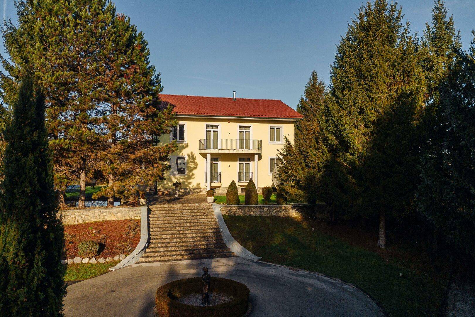 Eindrucksvolle Freitreppe führt zum Haupthaus, umgeben von einem kreisförmigen Vorplatz und Bäumen.