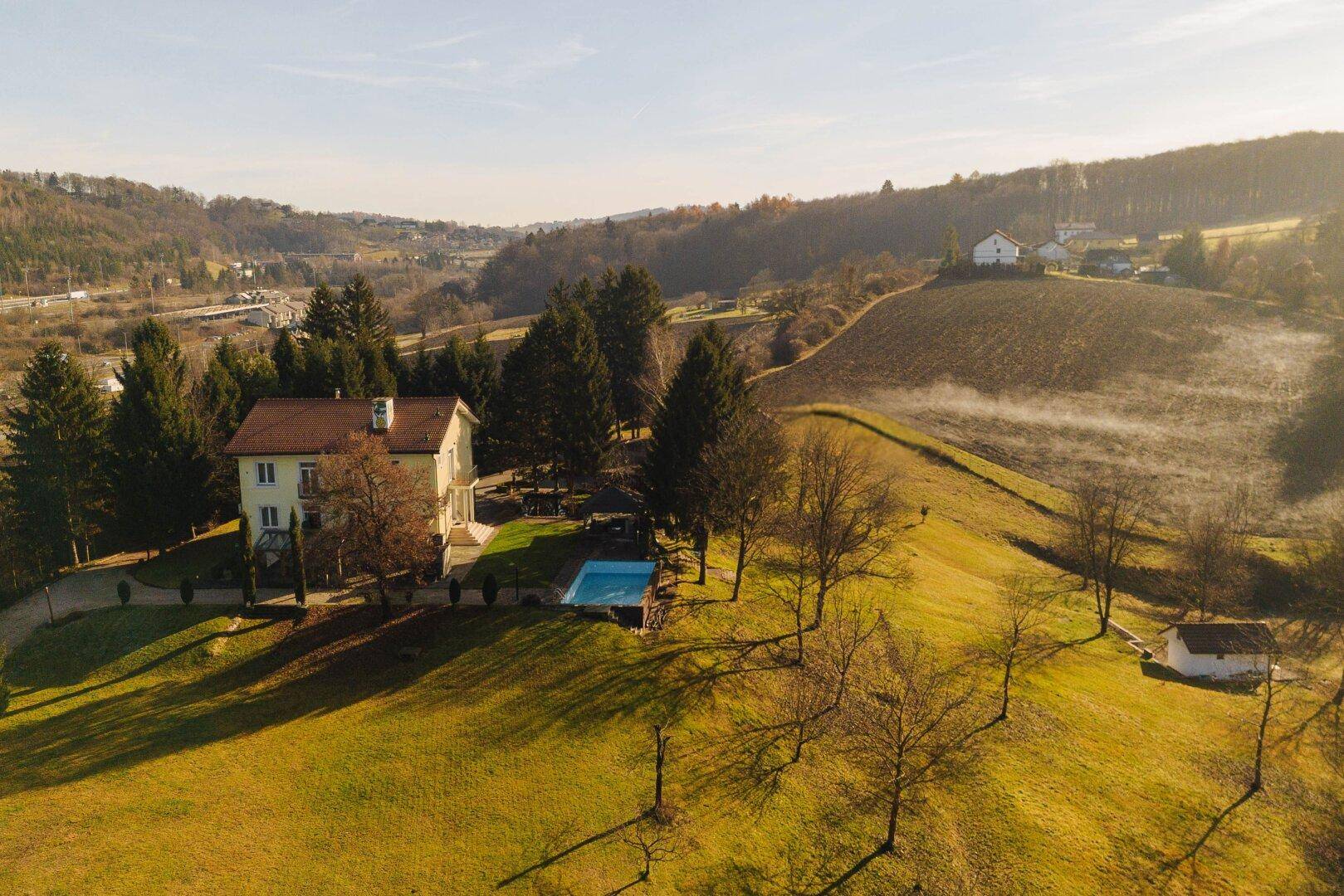 Nahaufnahme des Anwesens aus der Luft mit Haupthaus, Pool und grünen Hügeln.