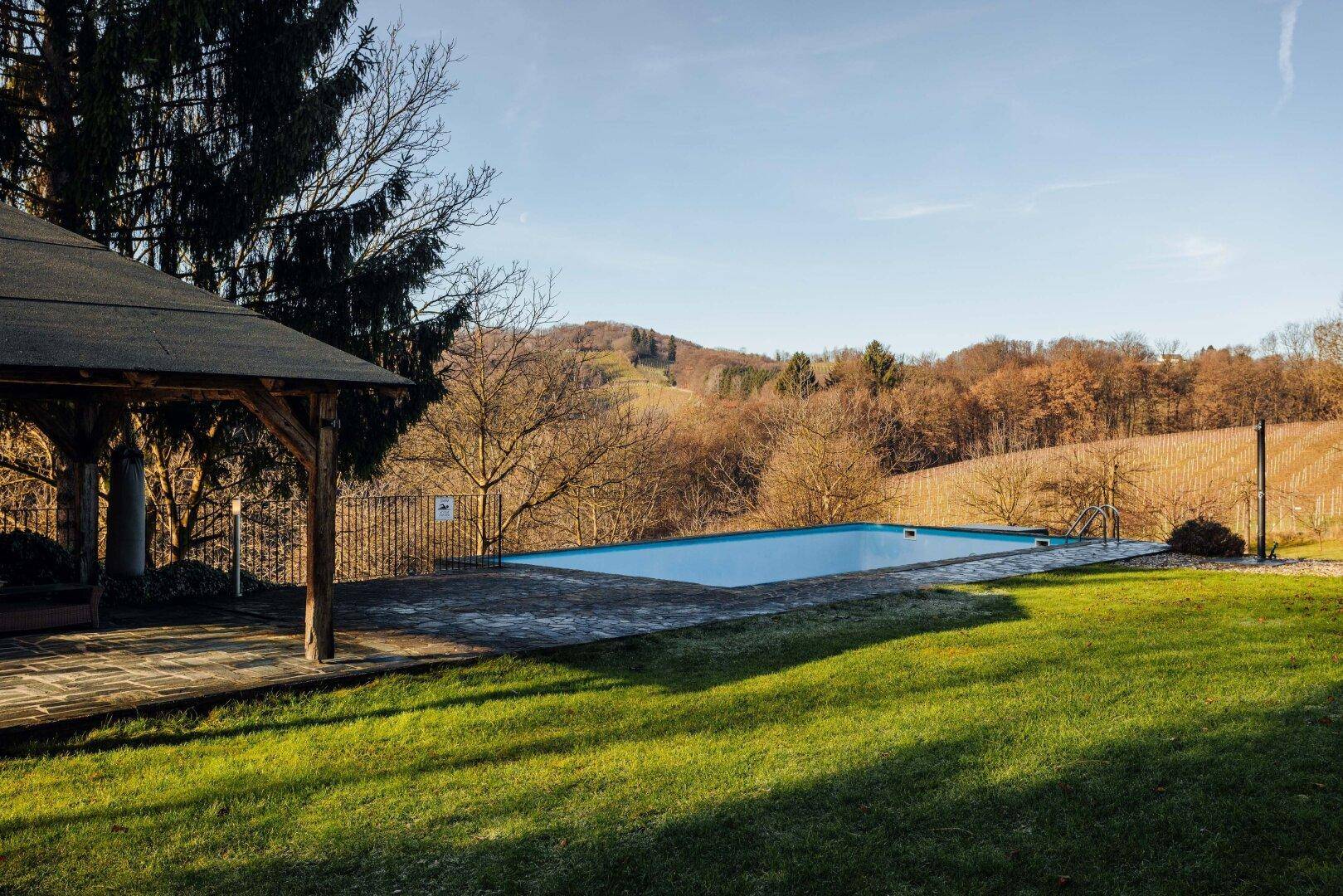 Entspannender Poolbereich im Garten mit einem Pavillon und Blick auf die grünen Hügel.