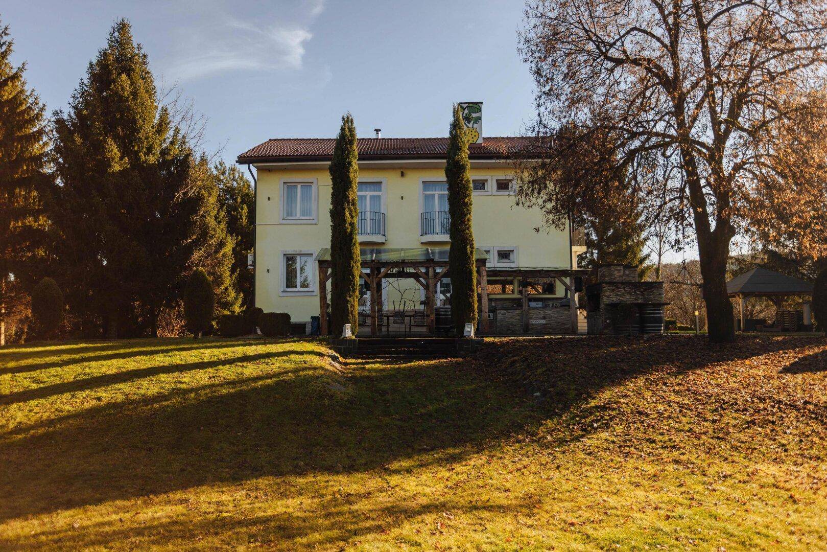 Das Haupthaus mit gelber Fassade, umgeben von hohen Bäumen und einer weitläufigen Rasenfläche.