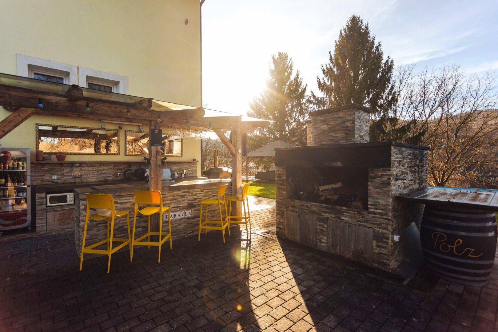 Moderne Außenküche mit gelben Barhockern, Grillbereich und sonniger Terrasse.