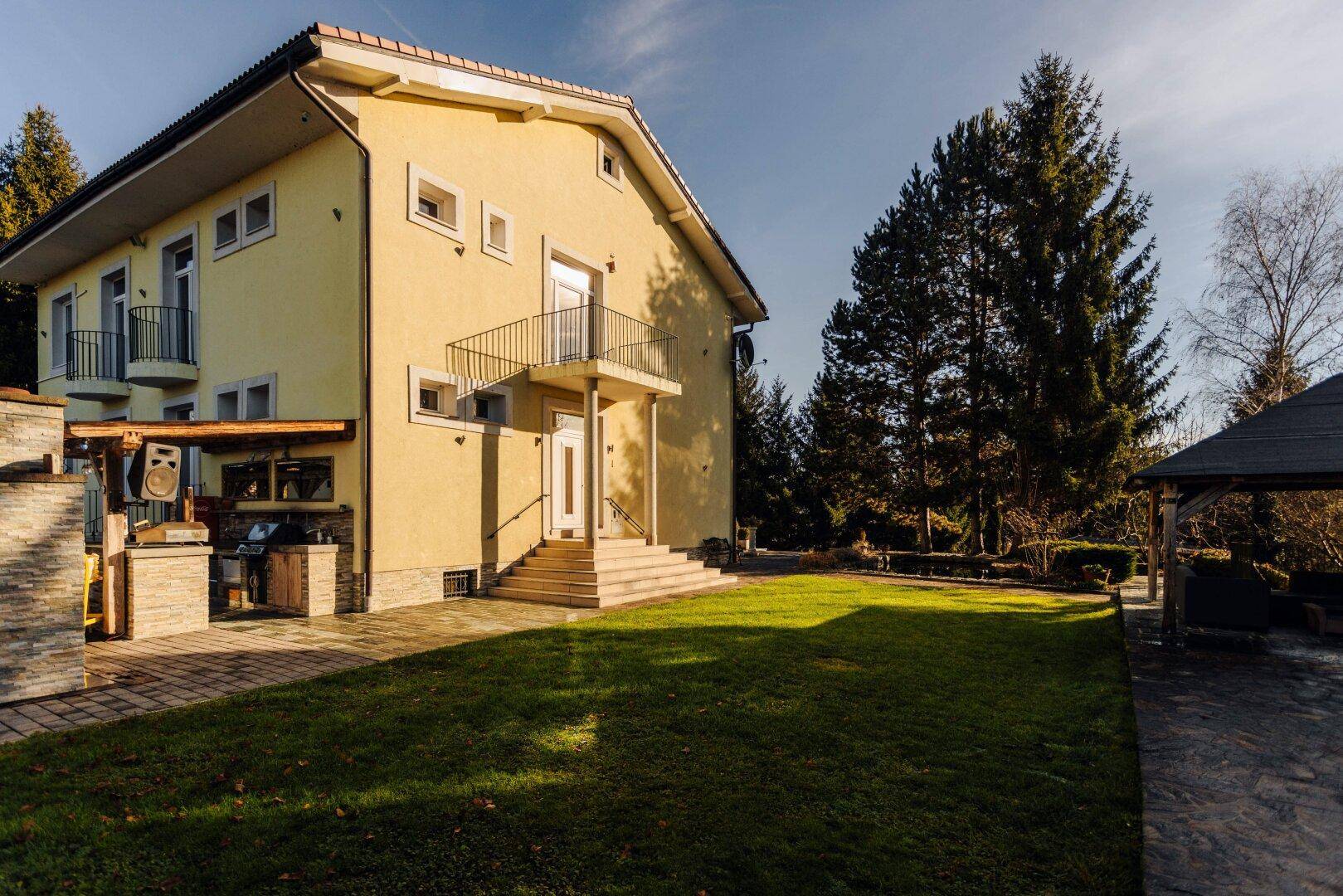 Das Haupthaus mit gepflegtem Rasen, umgeben von Bäumen und einem Pavillon im Hintergrund.