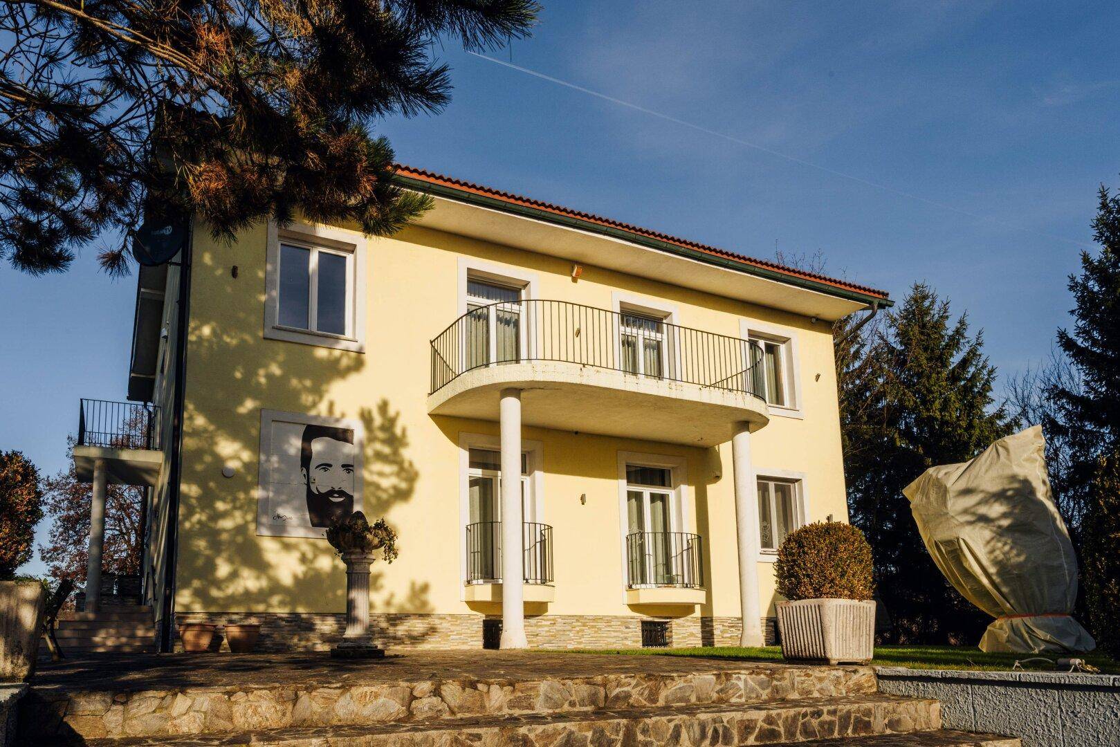 Das Haupthaus mit geschwungenem Balkon, einer großen Wandmalerei und sonniger Fassade.
