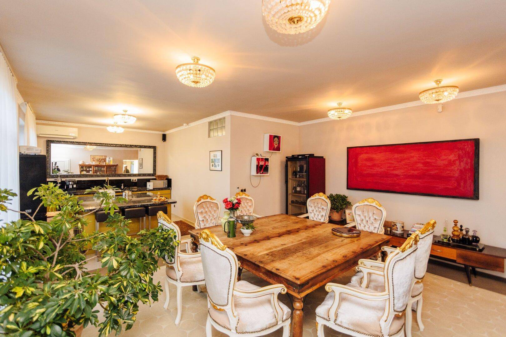 Eleganter Essbereich mit großem Holztisch, opulenten Stühlen und offener Küche im Hintergrund.