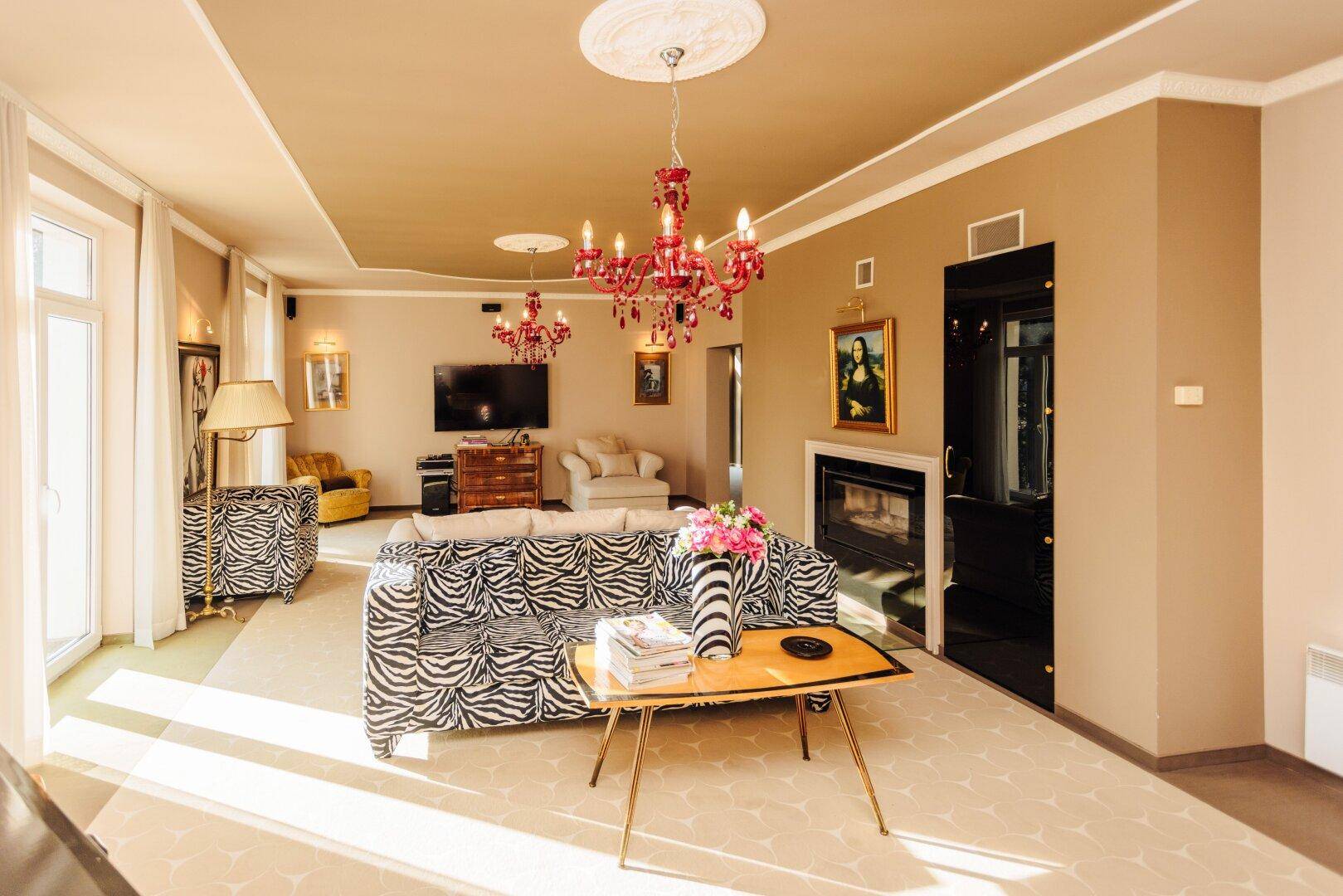 Extravagantes Wohnzimmer mit Zebra-Sofa, Kamin und auffälligen roten Kronleuchtern.