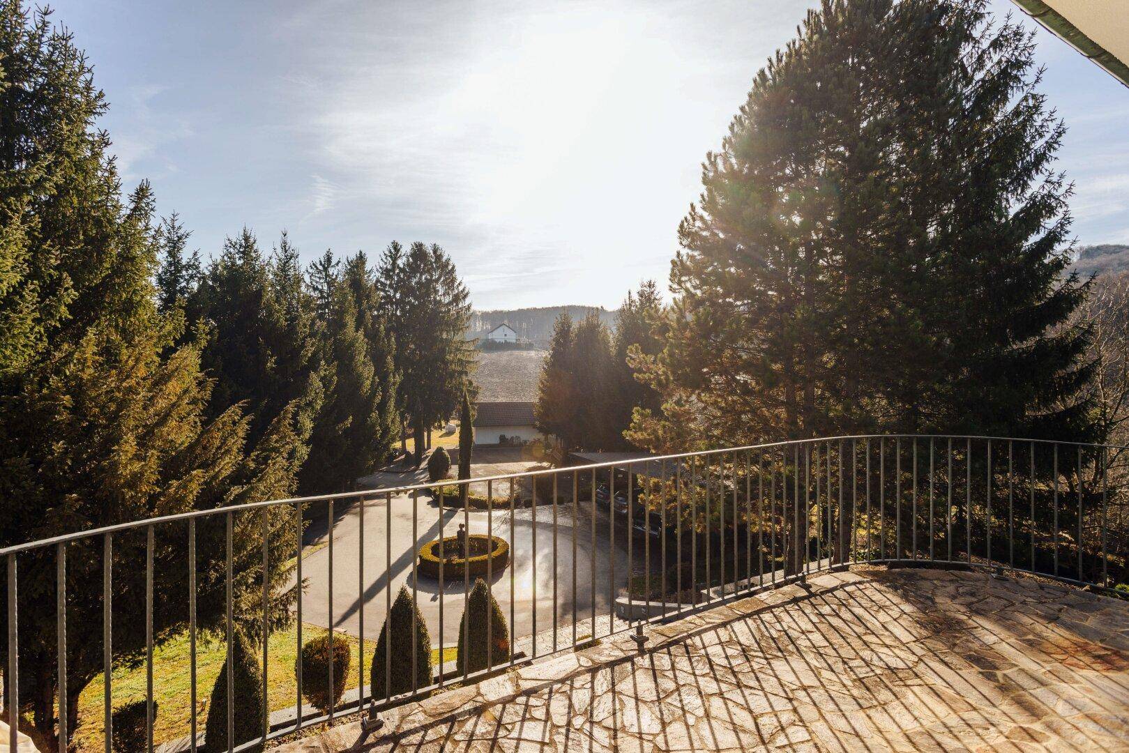 Großer Balkon mit Steinboden und weitem Blick auf den Vorplatz und die Baumlandschaft.
