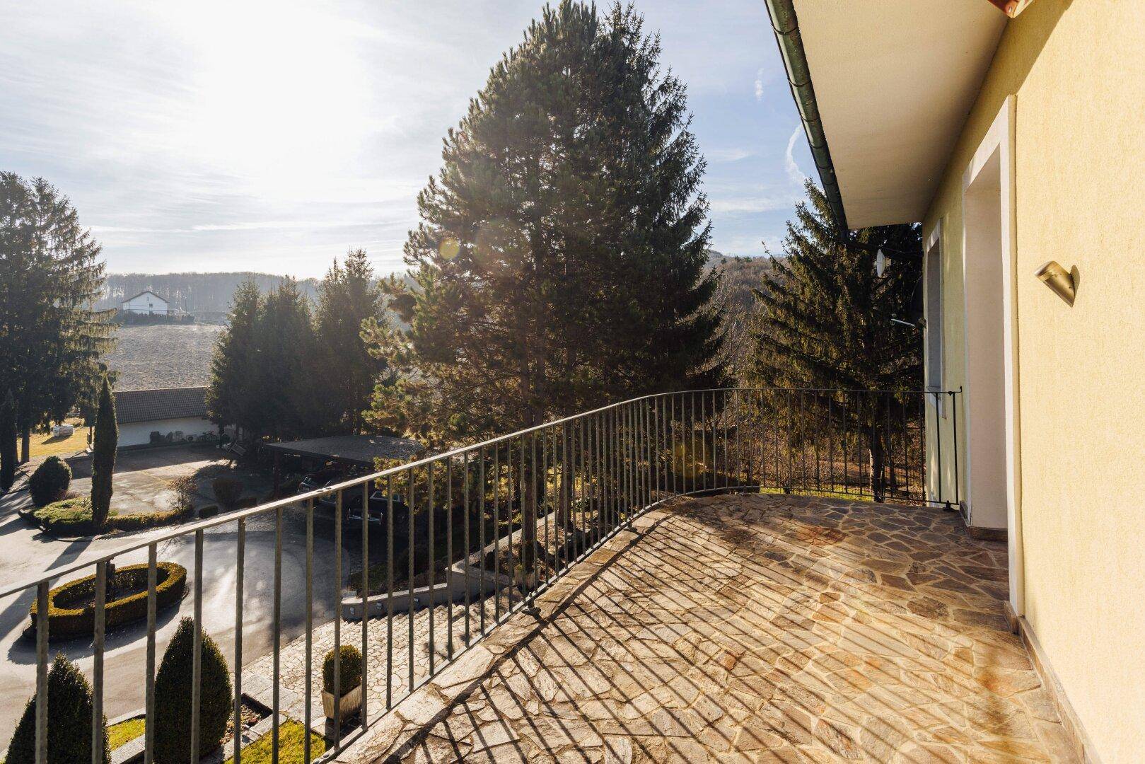 Geräumiger Balkon mit Steinplatten und schmiedeeisernem Geländer, sonnig gelegen.