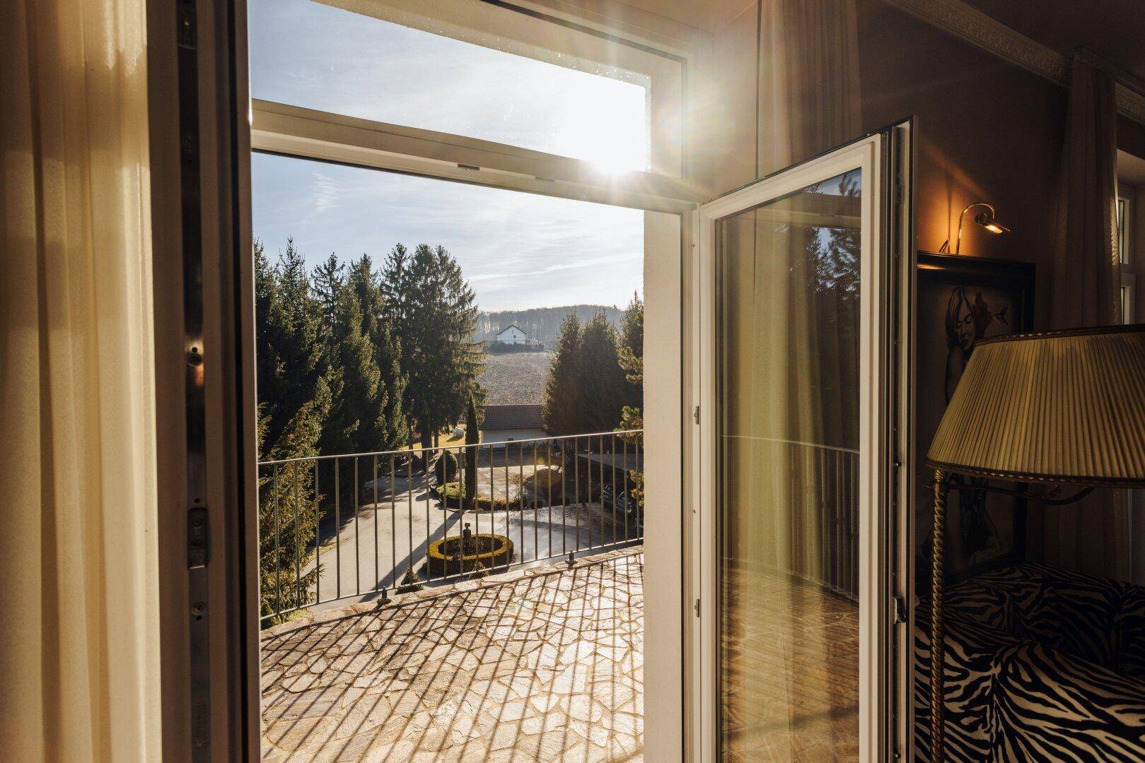 Blick aus dem Zimmer durch die offene Balkontür auf die sonnige Außenanlage.
