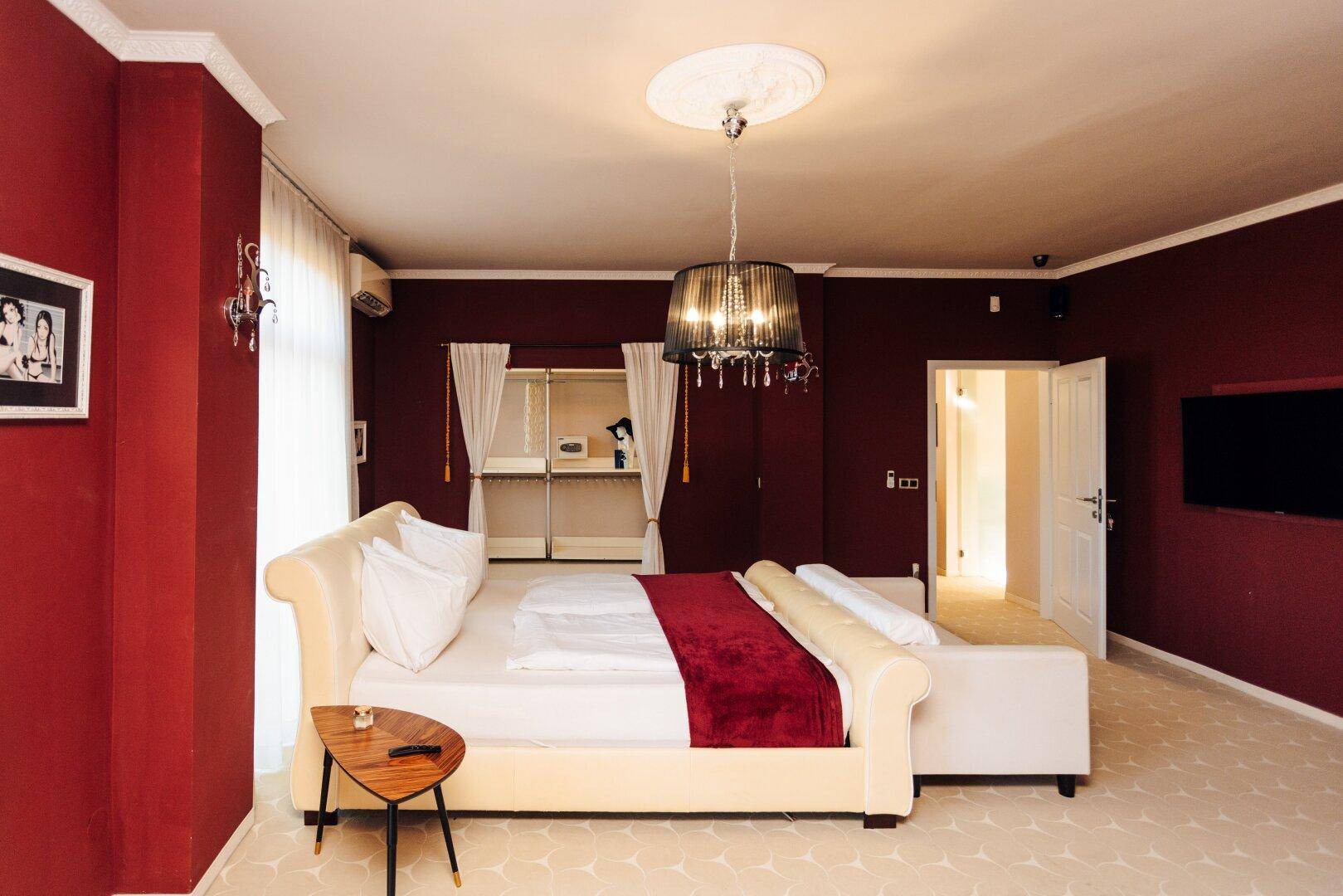 Schlafzimmer mit roten Wänden, Bett und offenem Ankleidebereich mit Regalsystem.