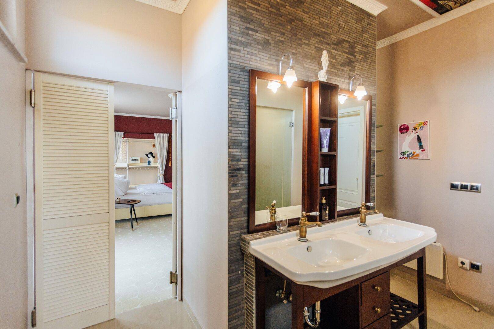 Badezimmer mit Doppelwaschbecken, Steinakzentwand und Zugang zum Schlafzimmer.