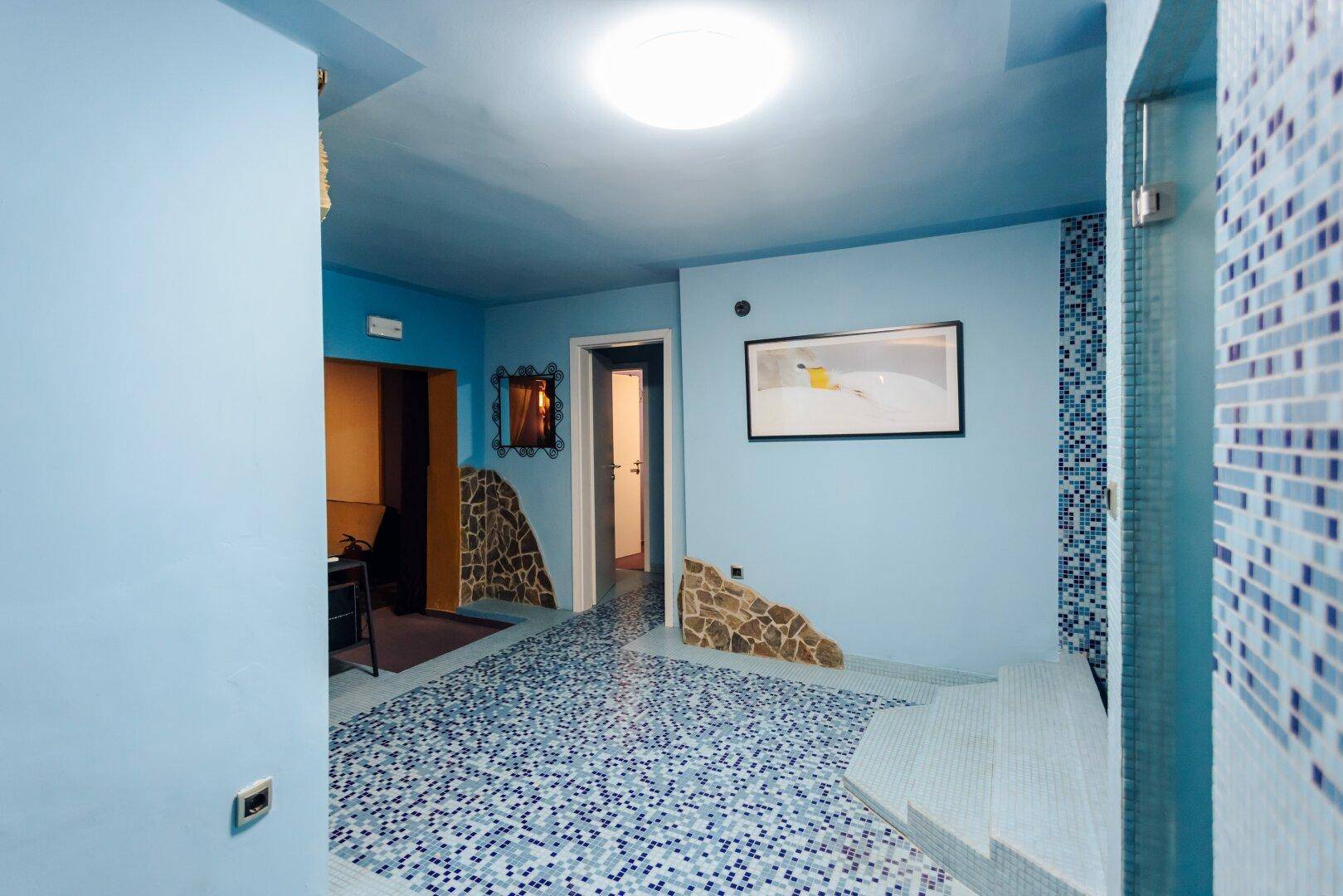 Blauer Wellnessbereich mit Mosaikfliesen und Stufen, die zu einem Badebereich führen.