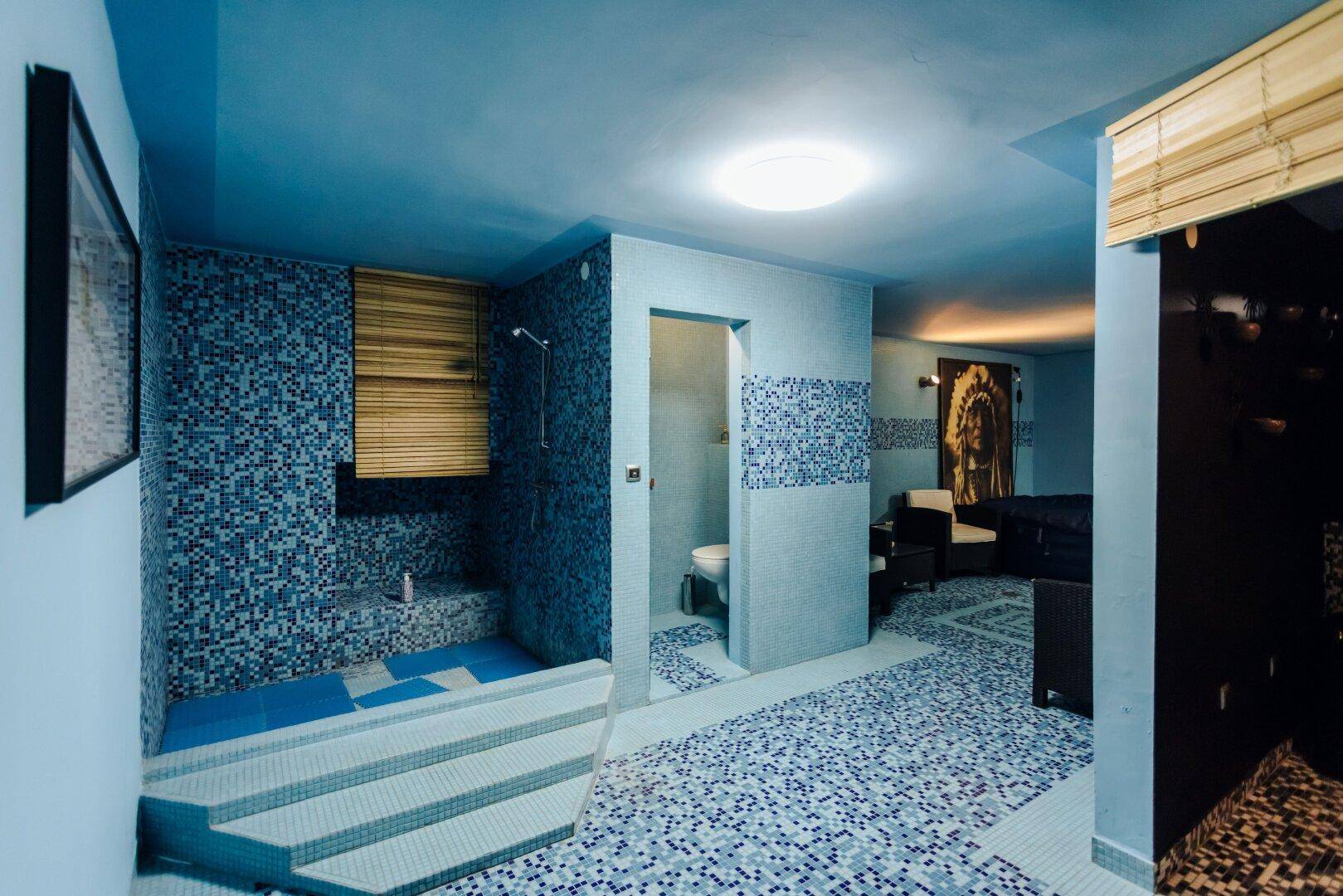 Wellnessbereich mit blauen Mosaikfliesen, Dusche und separatem WC-Bereich.