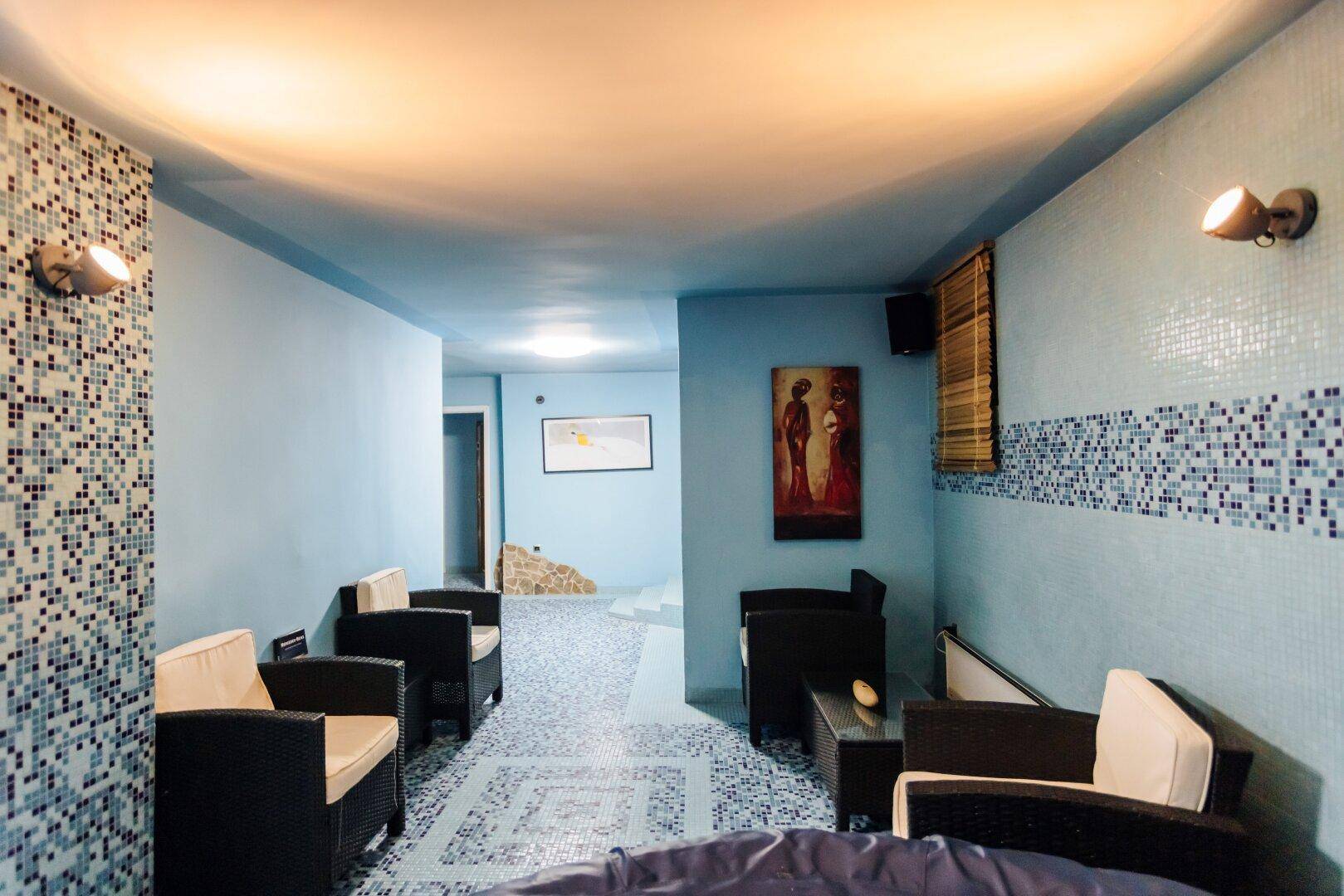 Blauer Wellnessbereich mit Mosaikfliesen, bequemen Sitzgelegenheiten und stimmungsvoller Beleuchtung.