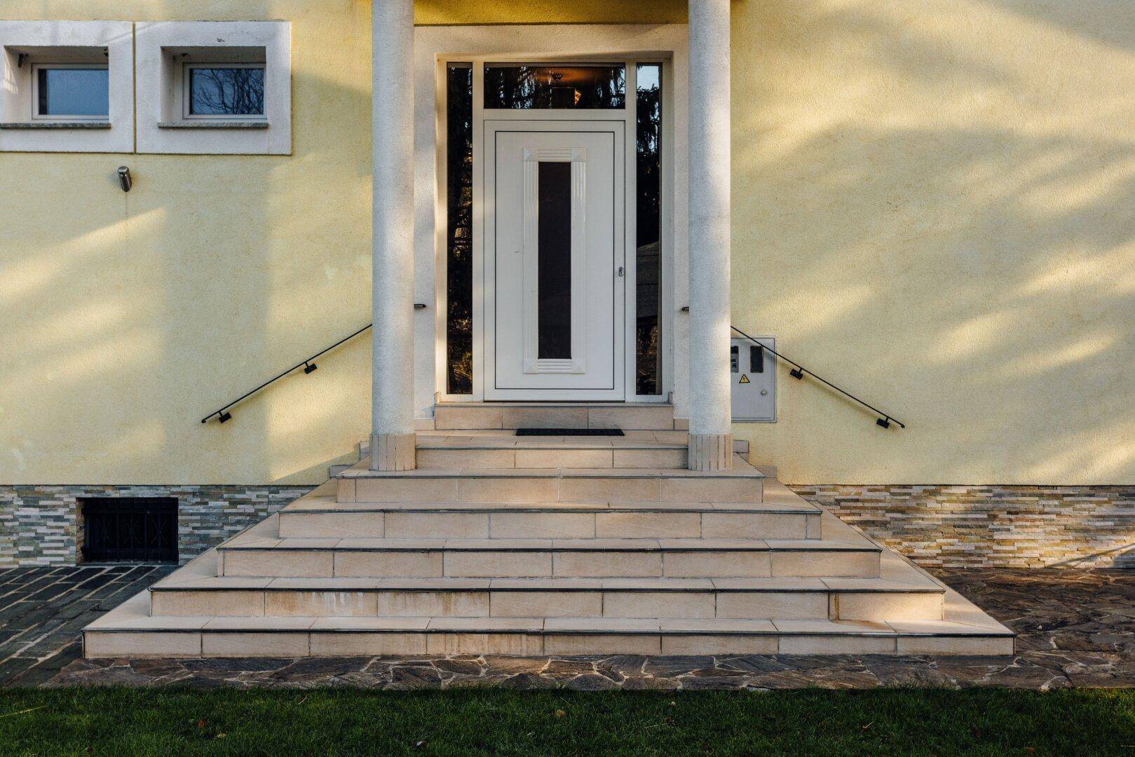 Haupteingang des Hauses mit breiter Steintreppe und eleganten Handläufen.