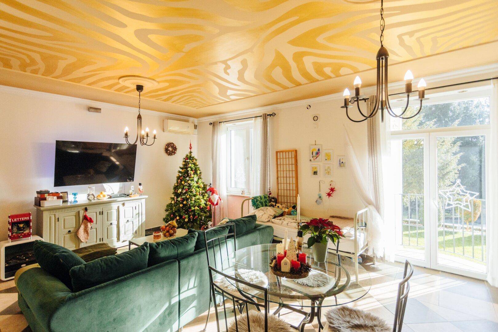 Festlich dekoriertes Wohnzimmer mit Weihnachtsbaum, grünem Sofa und auffälliger Deckenmalerei.