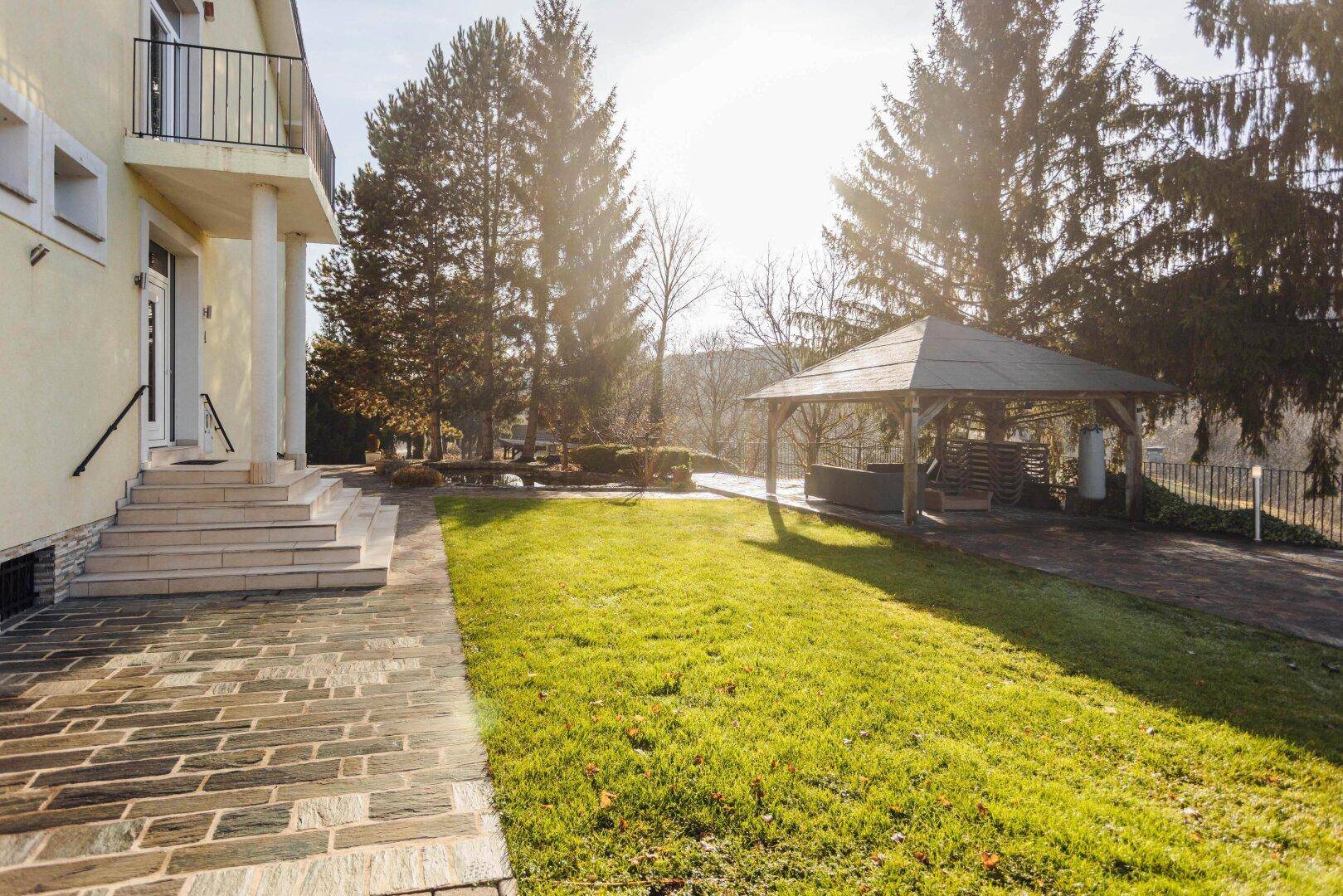 Seitenansicht des Hauses mit gepflegtem Rasen und einem Pavillon im sonnigen Garten.
