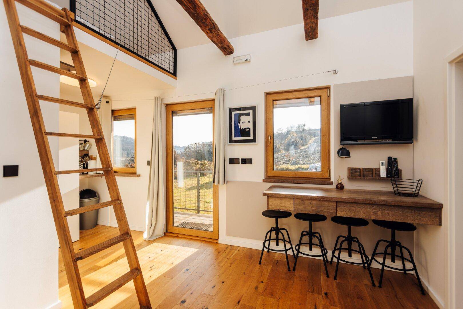 Arbeitsbereich im Gästehaus mit Schreibtisch, Hockern und weitem Blick in die Natur.