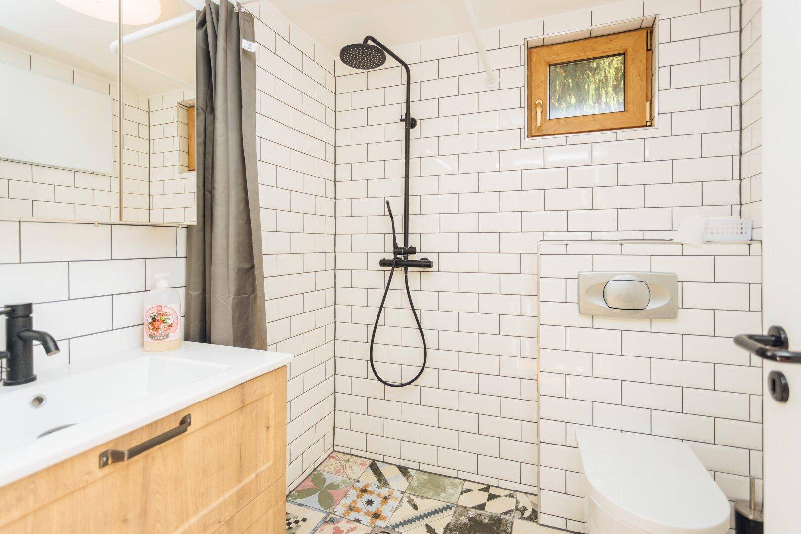 Modernes Badezimmer im Gästehaus mit weißen Fliesen, Dusche und Fenster.