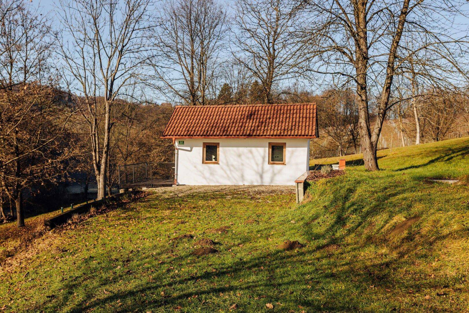 Kleines weißes Haus mit rotem Dach auf einem grünen Hügel in sonniger Landschaft.