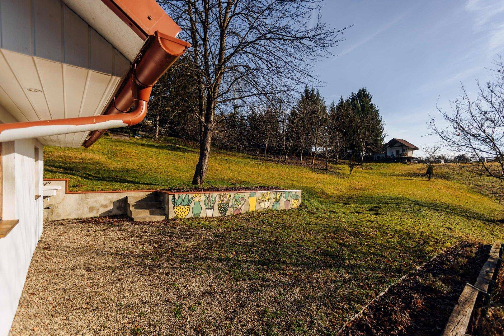 Gartenbereich mit bemalter Mauer und Blick auf die grüne Hügellandschaft.