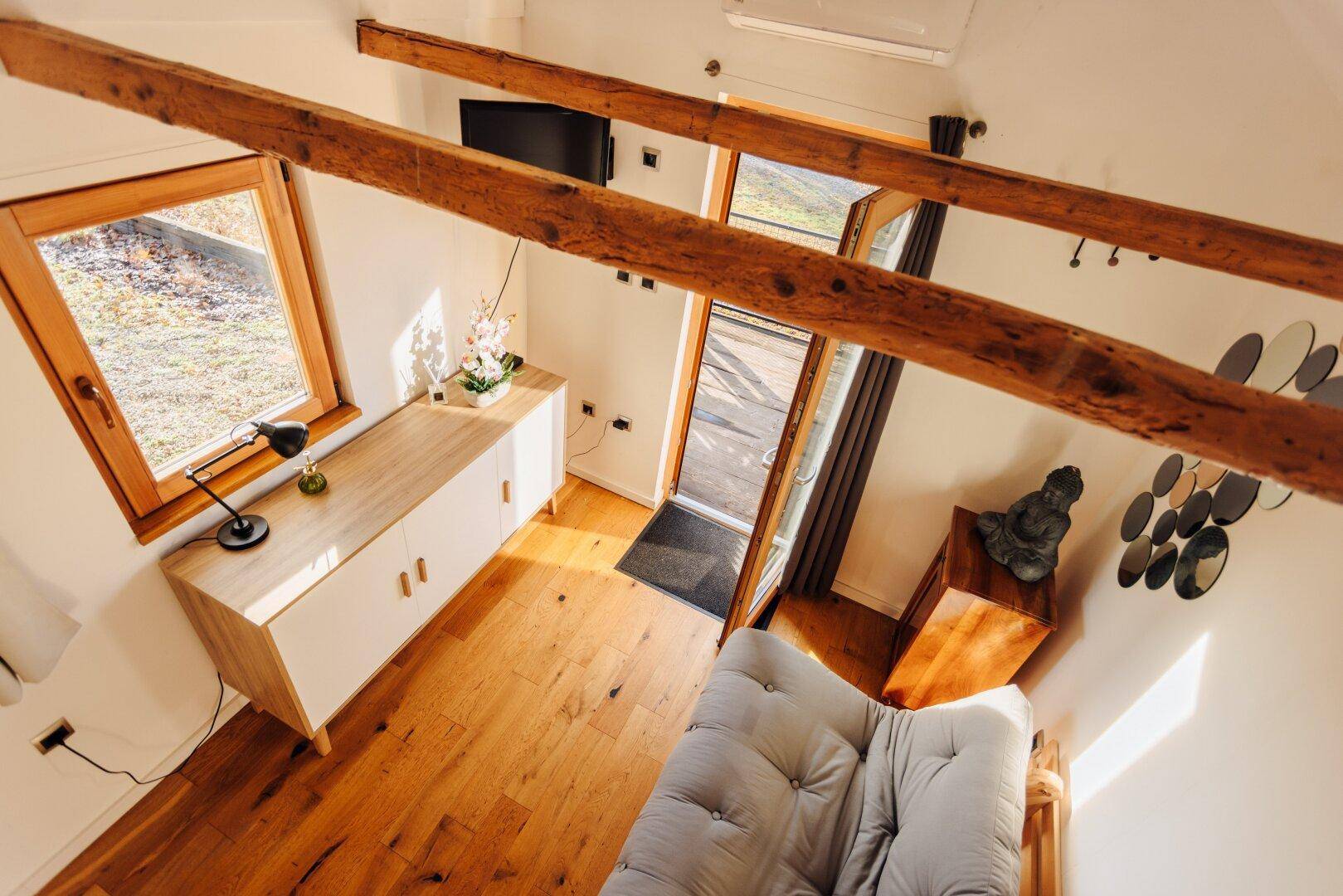 Blick von oben auf den Wohnbereich des Gästehauses mit Holzbalken und Sofa.