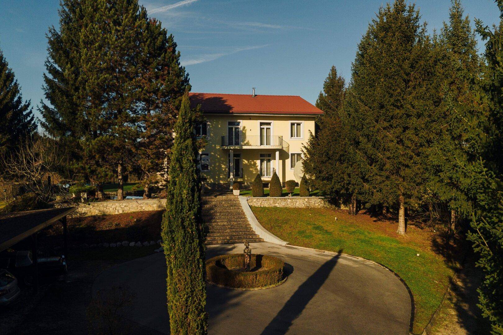 Das Haupthaus von vorne, umgeben von hohen Bäumen und einem gepflegten Vorplatz.
