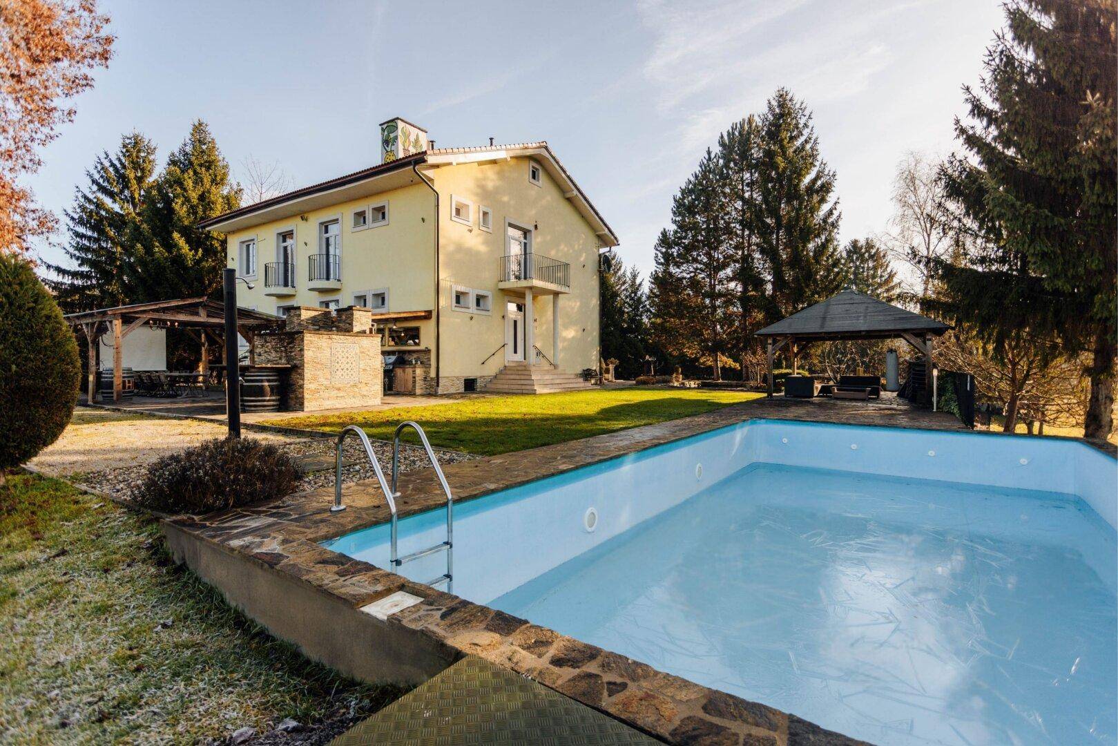 Das Haupthaus mit gelber Fassade und rotem Dach, umgeben von Grünflächen und einem Pool.