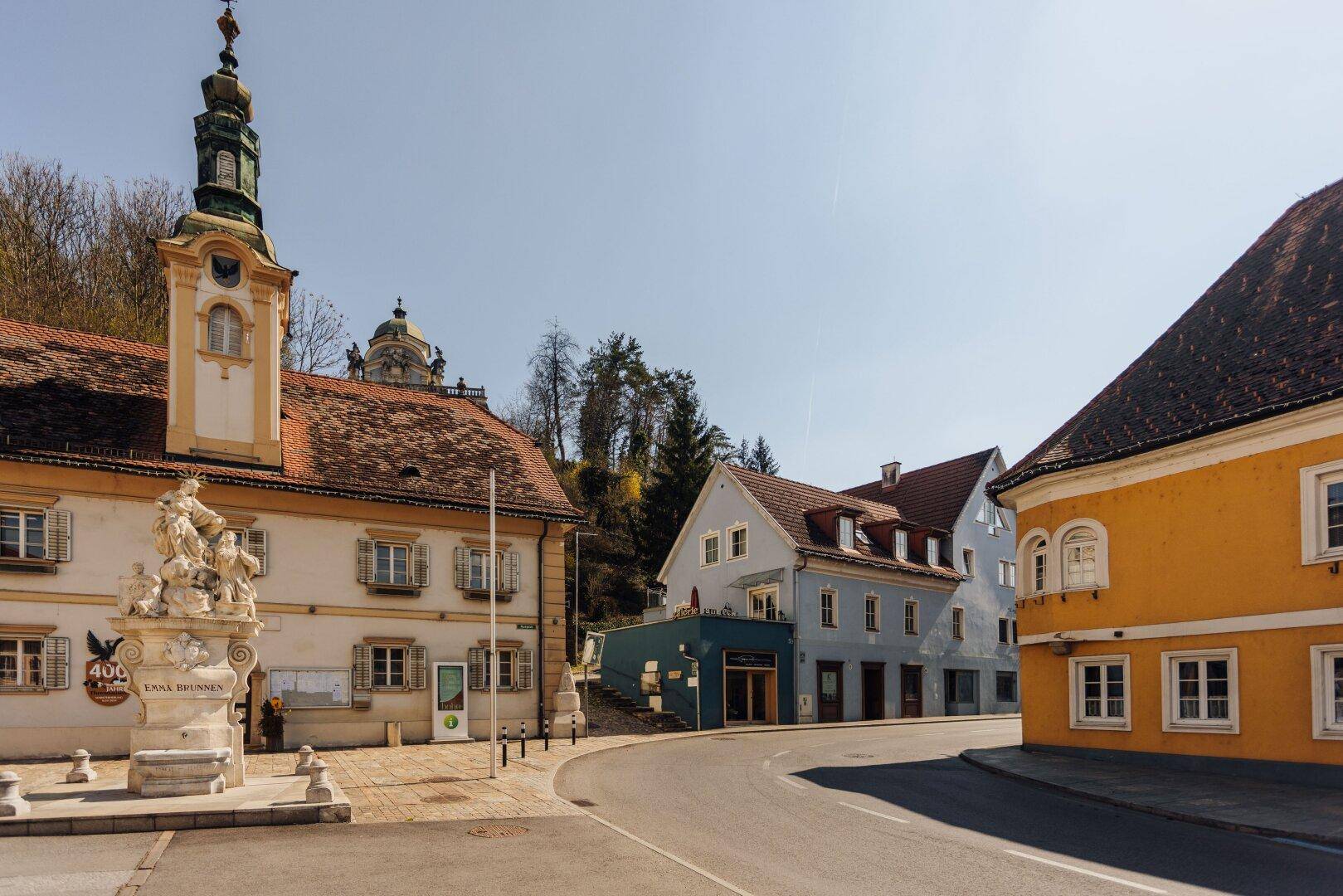 Historische Straße mit einem hellblauen Gebäude und einem markanten Kirchturm im Hintergrund.