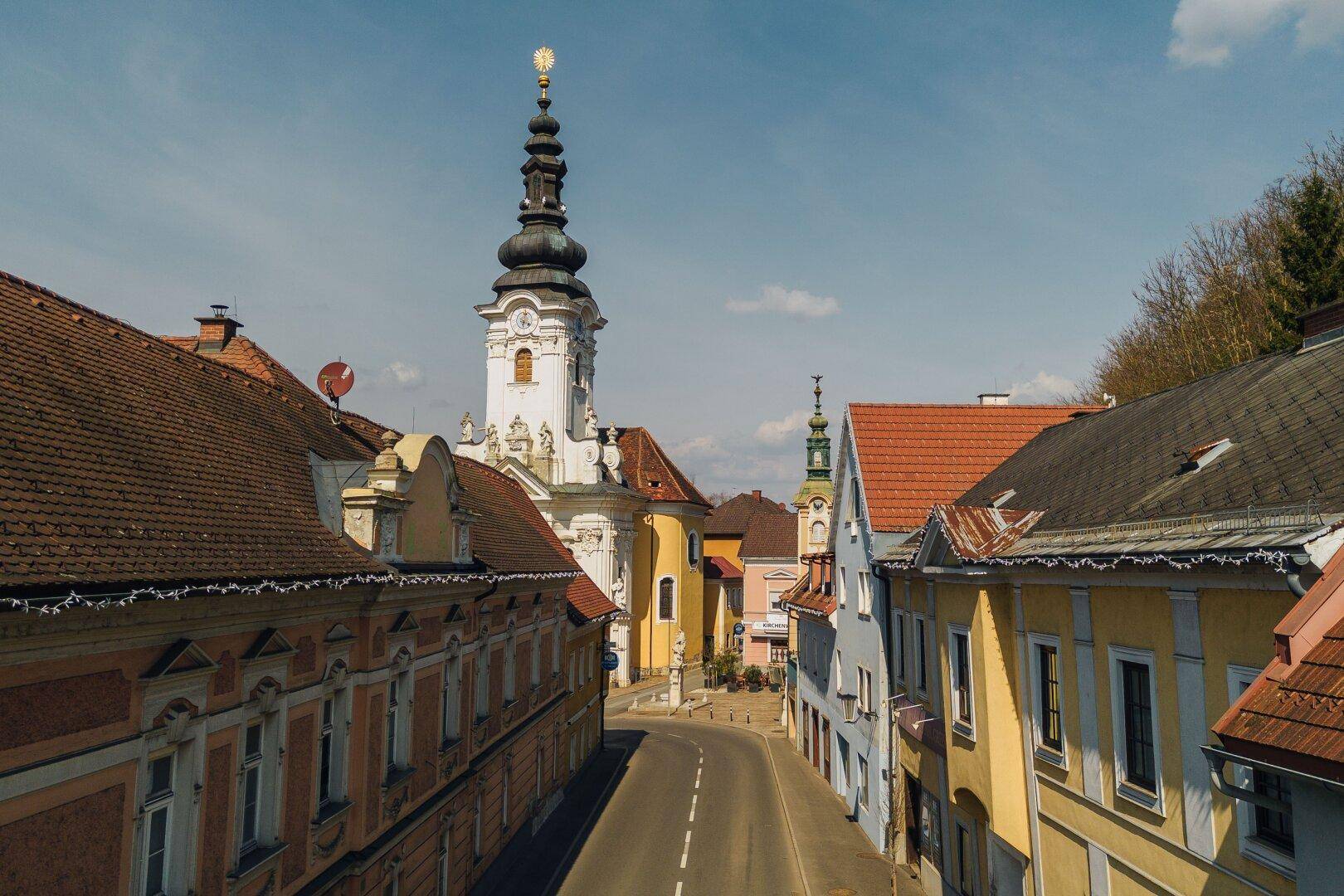 Blick von oben auf eine historische Straße, die zu einem imposanten weißen Kirchturm führt.