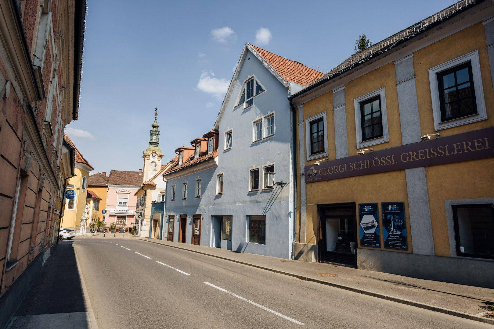 Historische Straße mit charmanten Gebäuden, darunter ein hellblaues Haus und ein gelbes Geschäft.