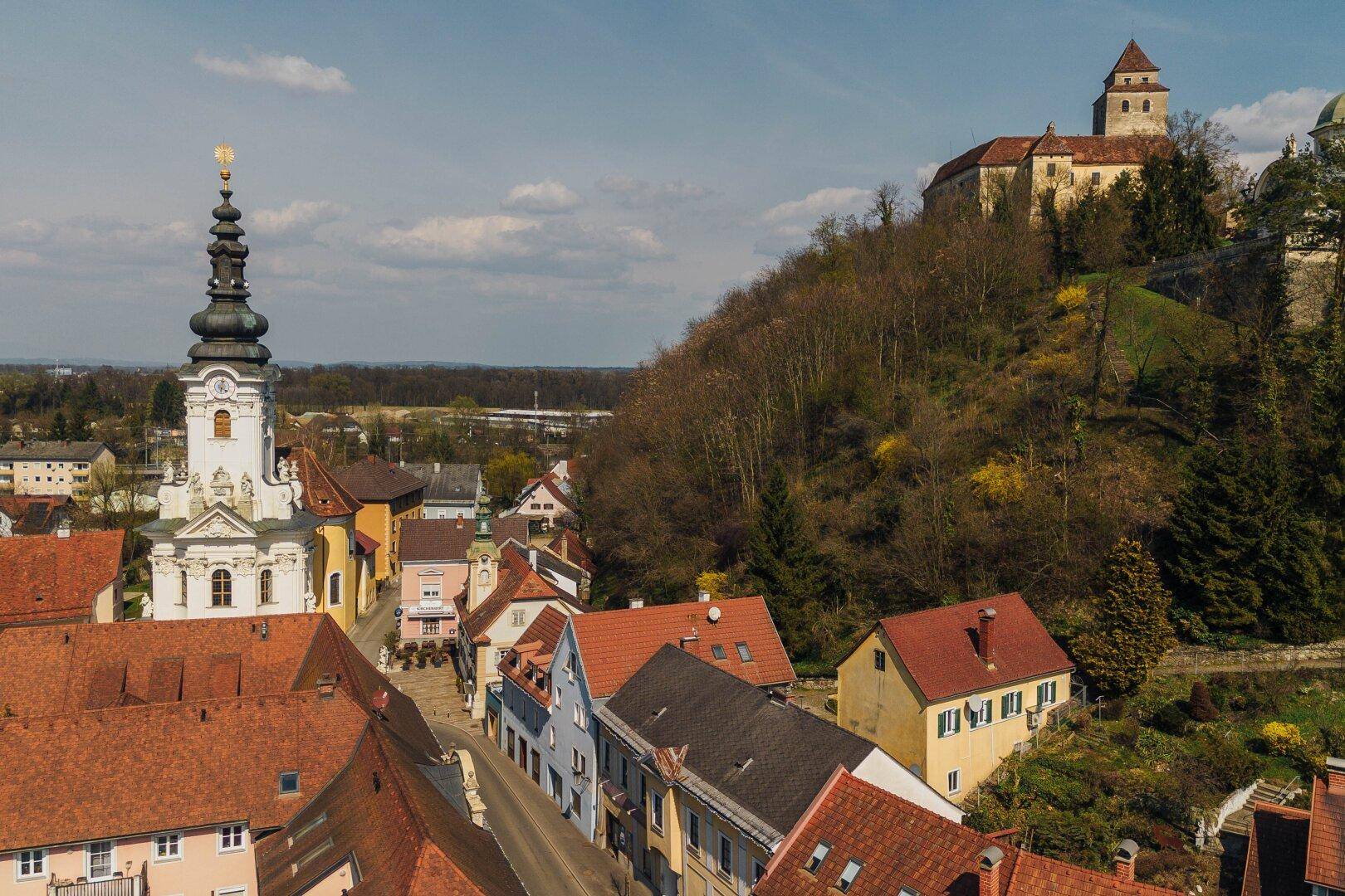Weitläufige Luftaufnahme der historischen Stadt mit Kirche und einer Burg auf dem Hügel.