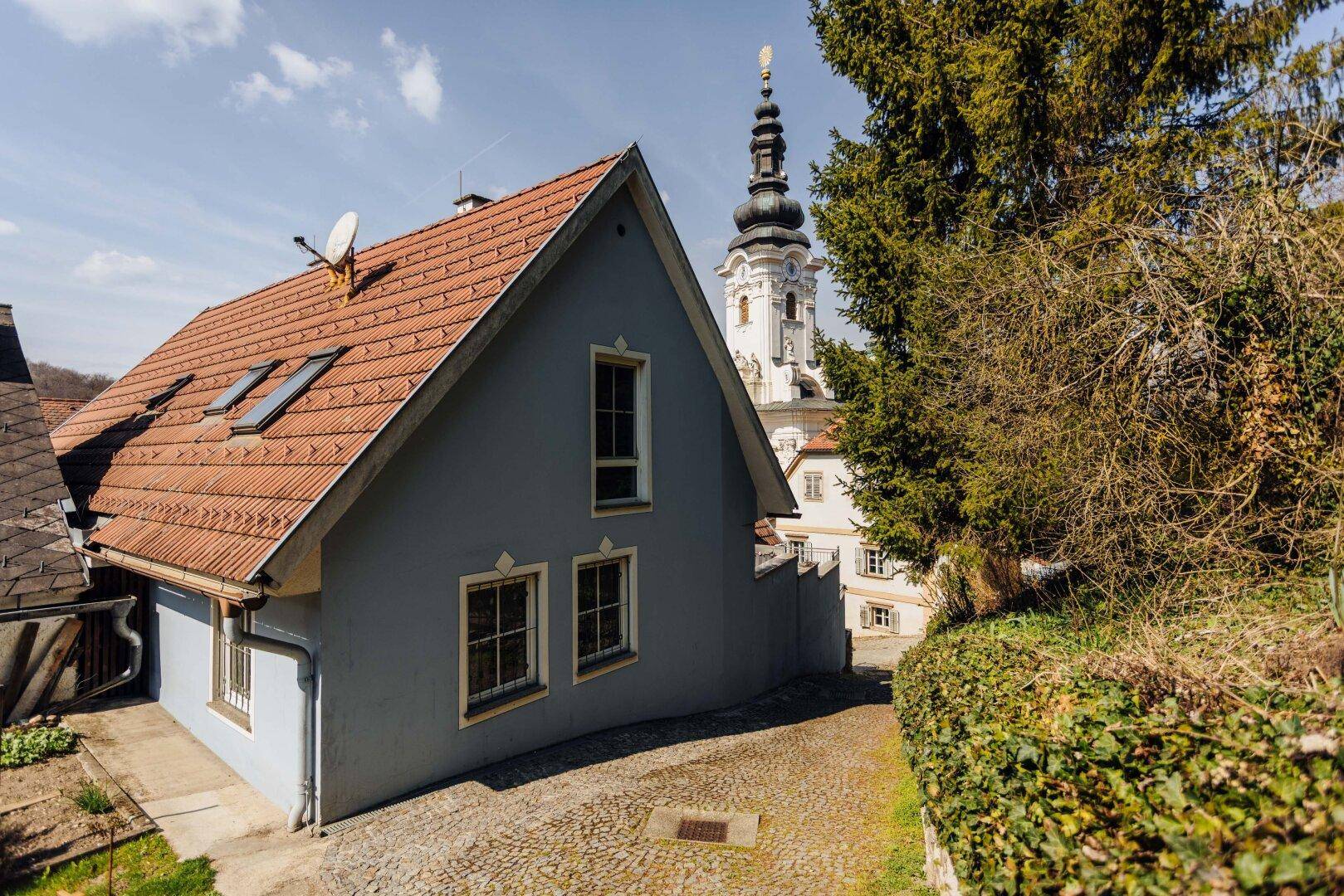 Seitenansicht des Gebäudes mit Dachfenstern und einem Weg, der zum Kirchturm führt.