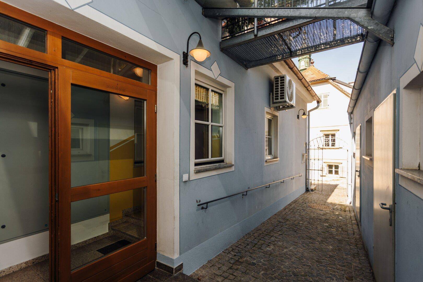Außenflur mit Holztür, Fenster und einer Klimaanlage an der Fassade des Gebäudes.