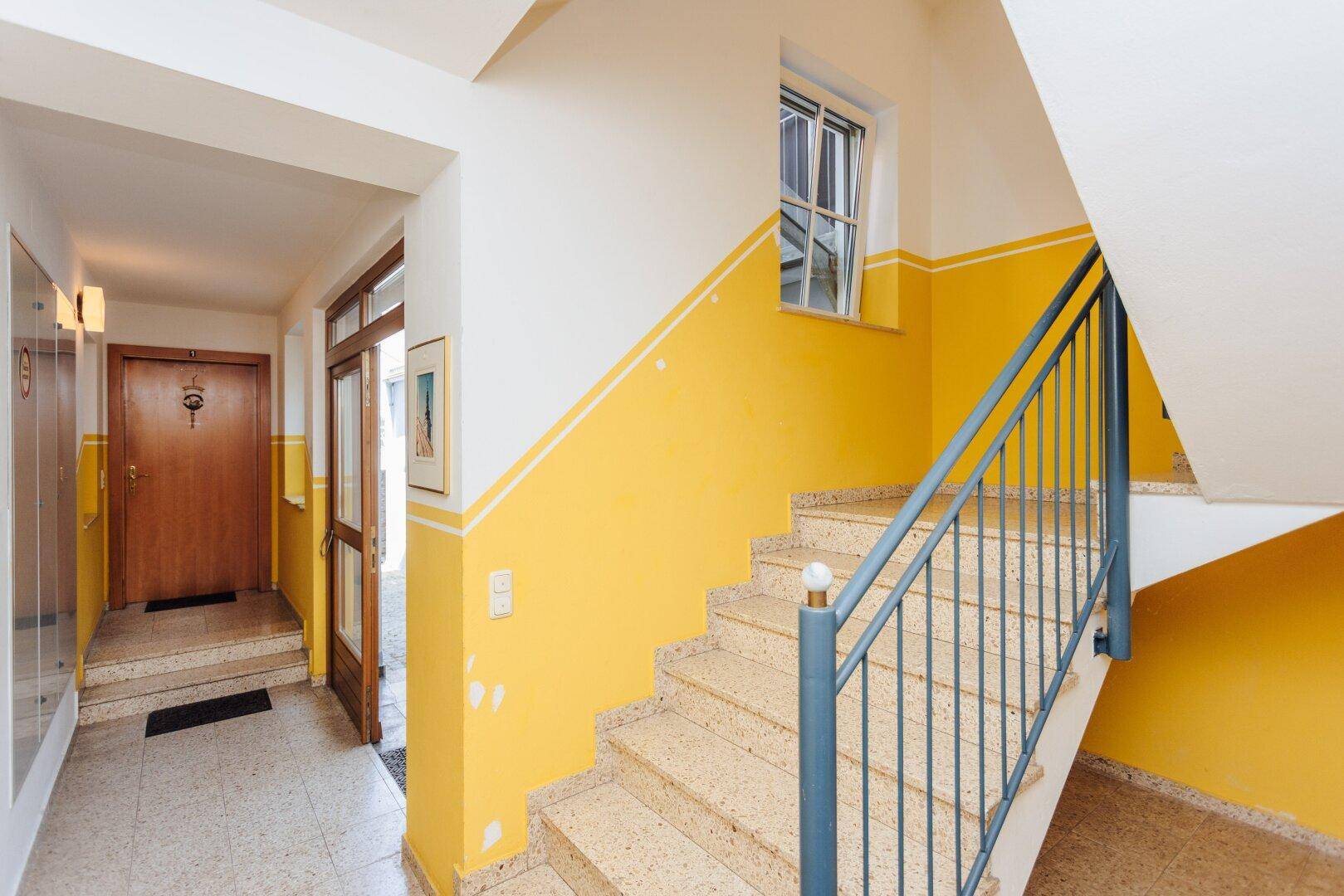 Heller Treppenaufgang mit gelb-weißen Wänden und Terrazzoboden in einem Mehrfamilienhaus.