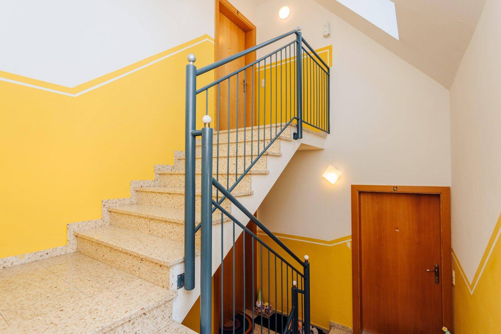 Treppenhaus mit gelb gestrichenen Wänden und einem stabilen Metallgeländer.